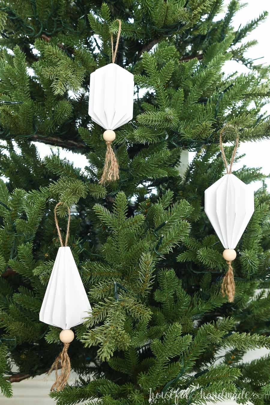 Three white paper Christmas ornaments in the shape of jewels with wood beads and tassels on the bottom.