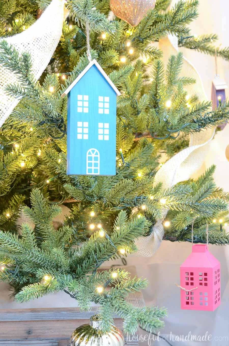 Close up of the tall blue scrap wood Christmas house hanging on a Christmas tree.