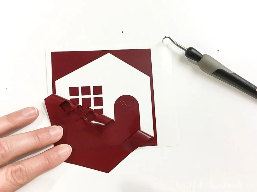 Dark red vinyl cut out with house template being weeded of the pieces you don't want.