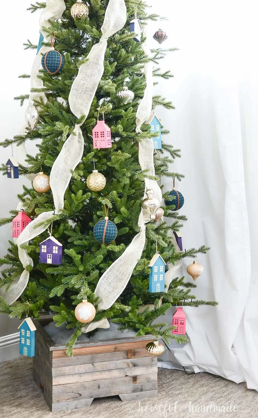 Showing some of the wood Christmas house ornaments made from scrap wood hanging on a Christmas tree decorated with jewel tones in a reclaimed wood Christmas tree stand.