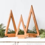 Three tabletop Christmas trees in a cluster with garland around the back.