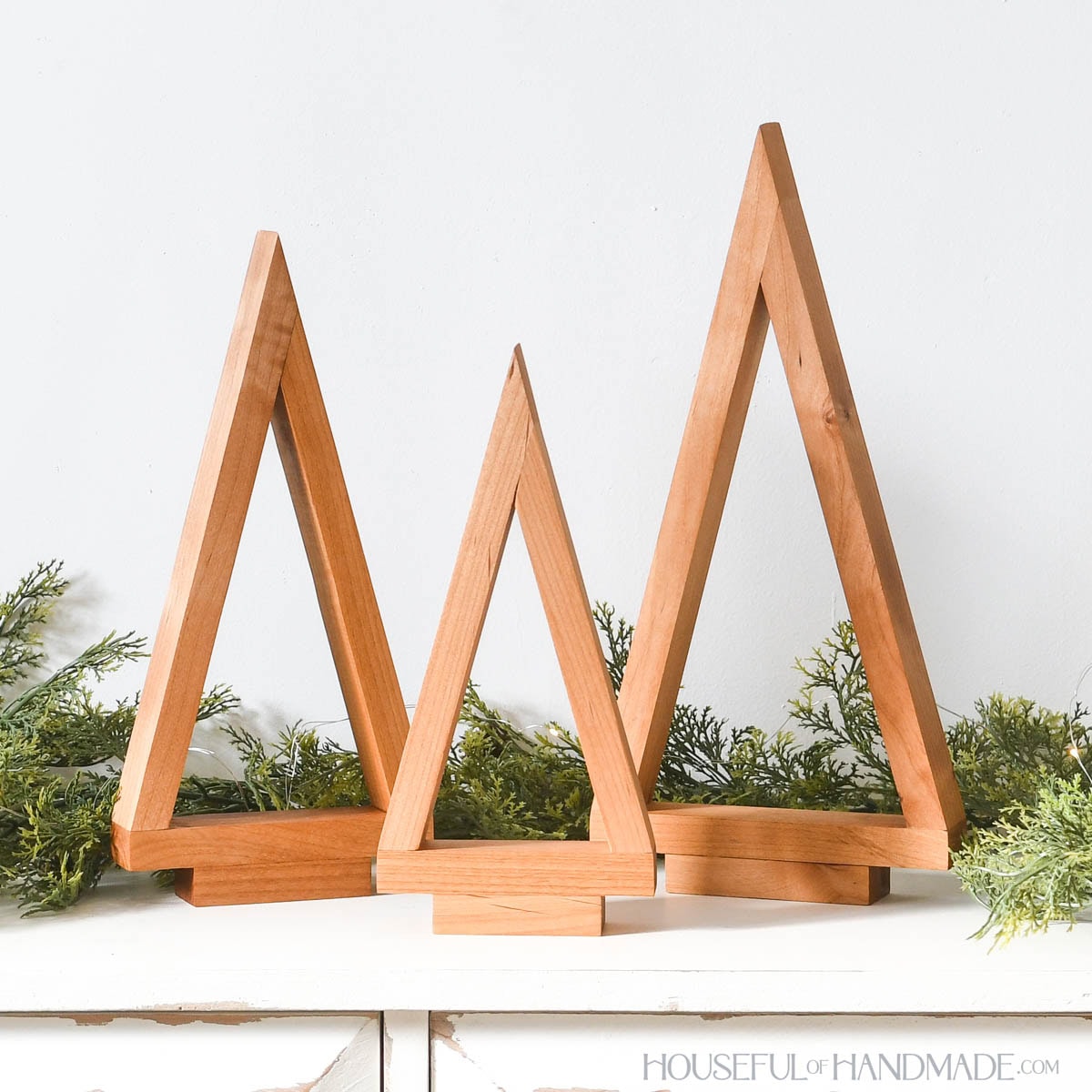 Three tabletop Christmas trees in a cluster with garland around the back.