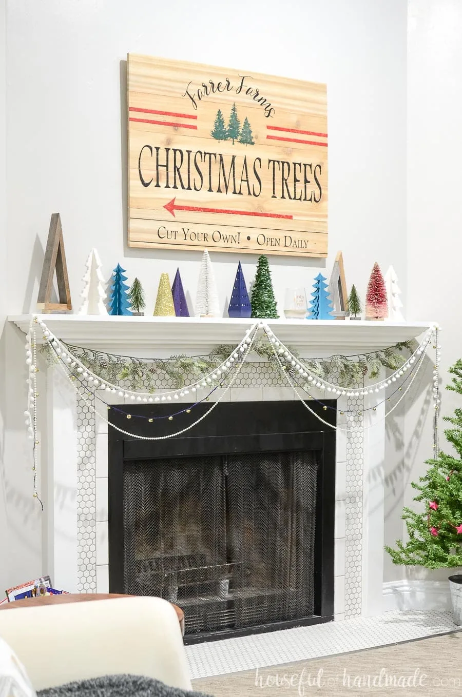 Christmas mantel decorated with reclaimed wood Christmas trees, porcelain Christmas trees and paper Christmas trees with a Christmas tree farm sign above it.