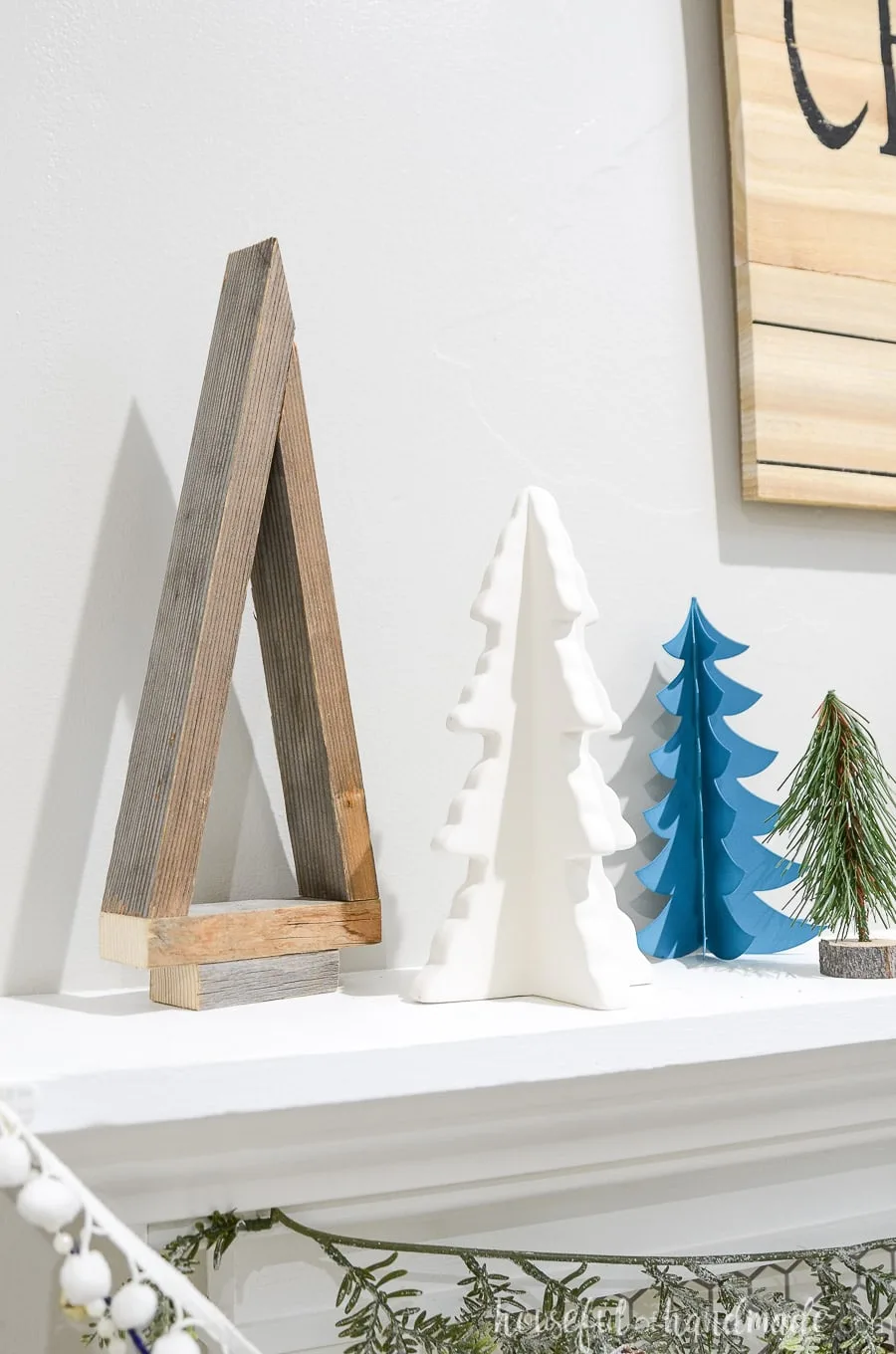 Reclaimed wood Christmas tree on a mantel next to other decorative Christmas trees.