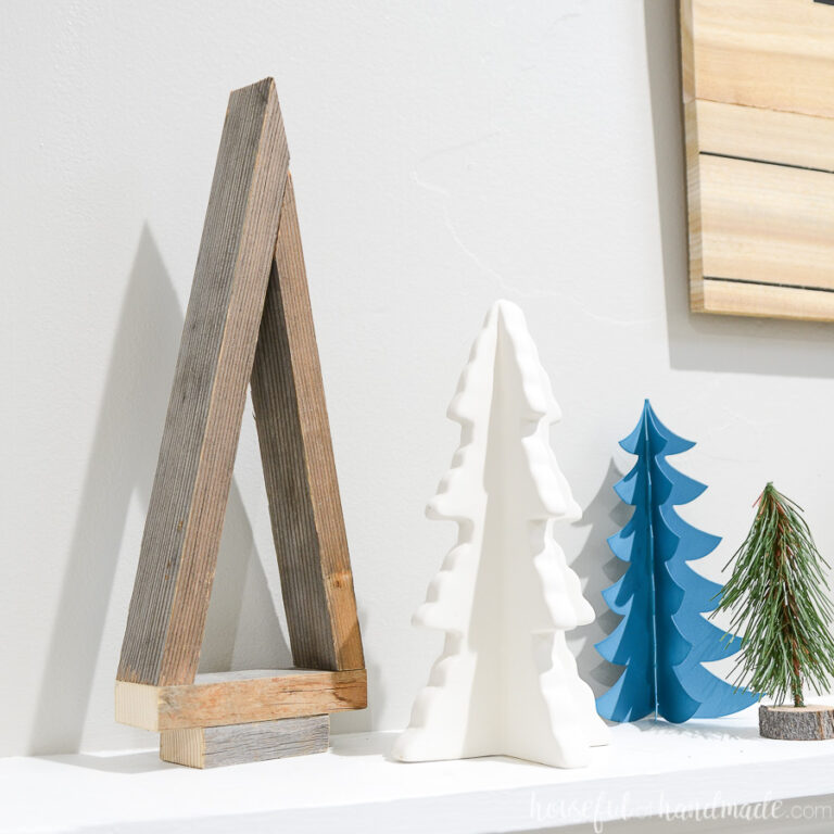 Simple decorative Christmas tree made from reclaimed wood on a mantle next to other decorative Christmas trees.