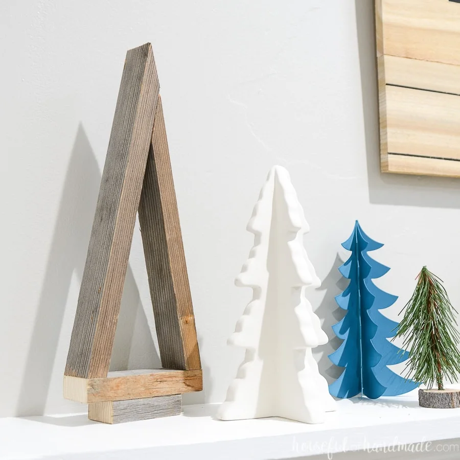 Simple decorative Christmas tree made from reclaimed wood on a mantle next to other decorative Christmas trees.