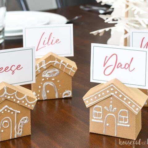 Four gingerbread place card holders made from paper on a table with family names on the place cards.