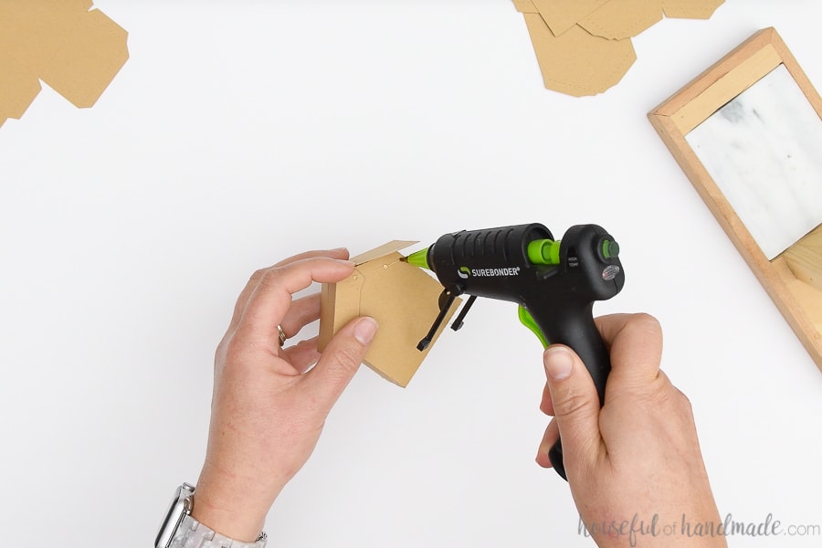 Adding drops of hot glue under the eave of the roof on the paper gingerbread house.