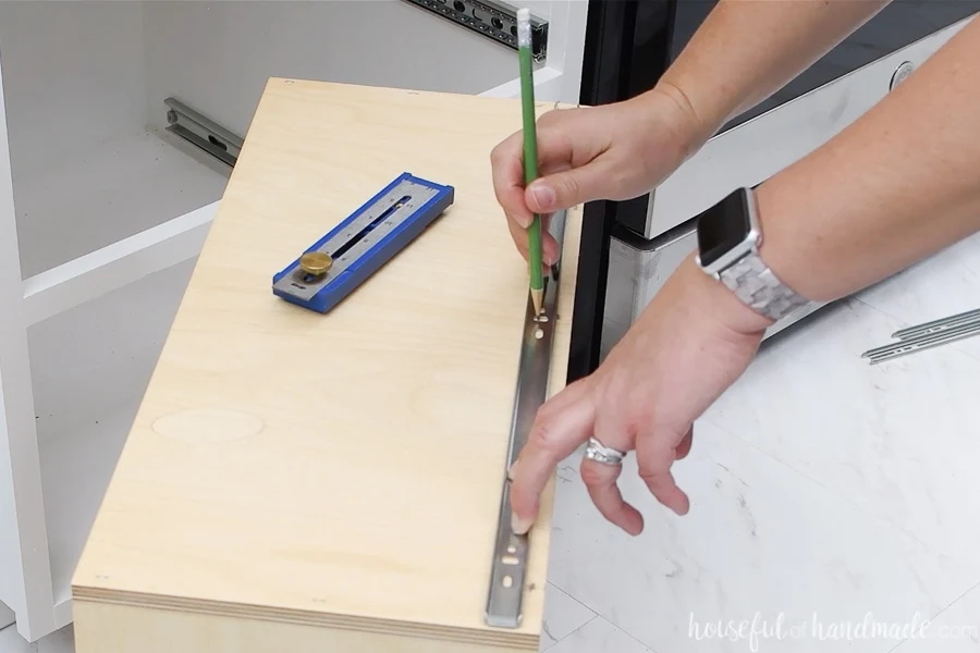 Marking where to drill pilot holes for the drawer slide piece attached to the drawer box with a pencil.