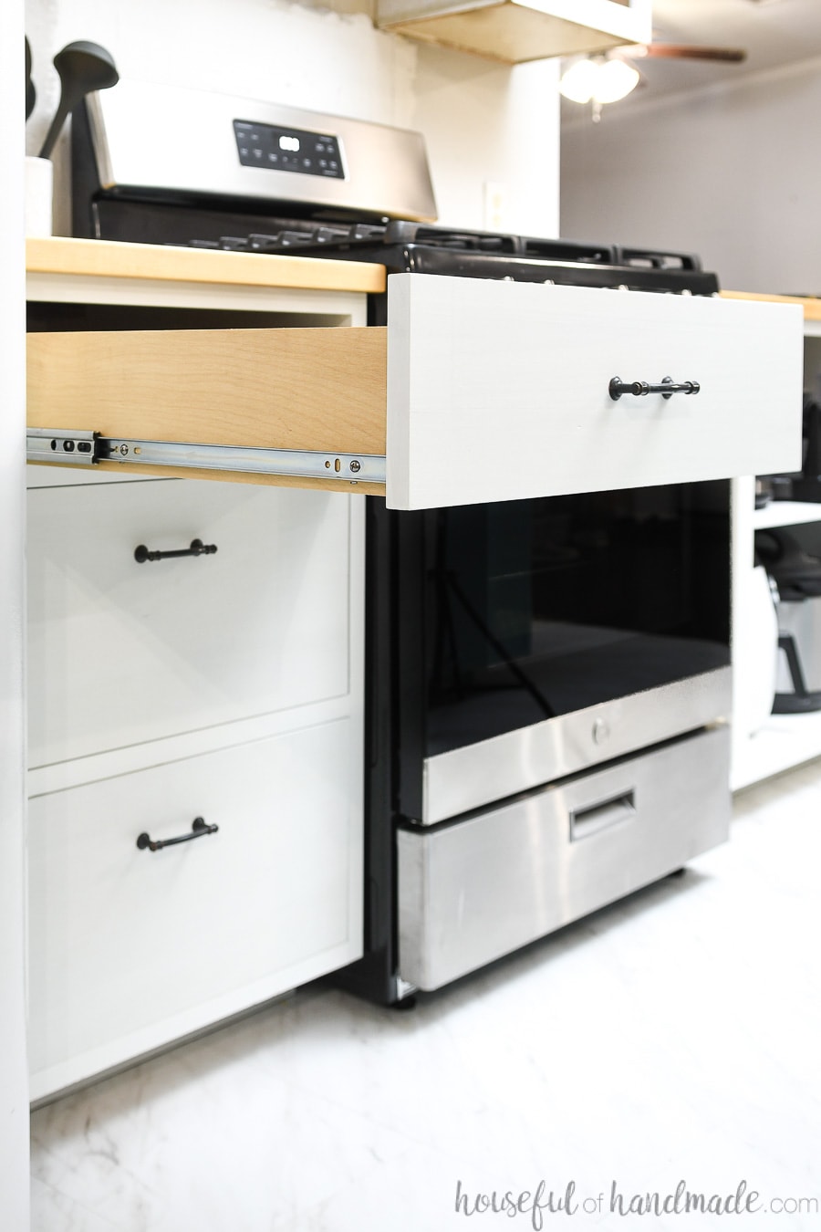 White drawer base cabinet next to a range that has the top drawer open showing the drawer slides on the side. 