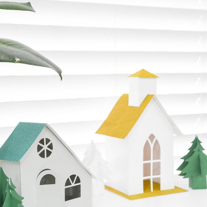 Two paper Christmas houses, one modern style and one church, on a console table.