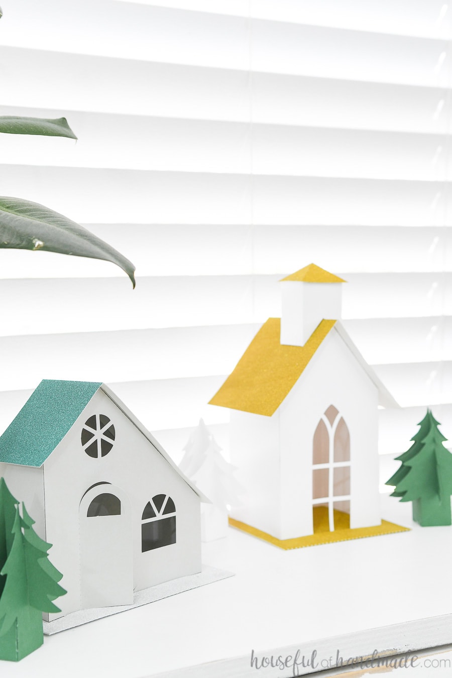 Two paper Christmas houses, one modern style and one church, on a console table.