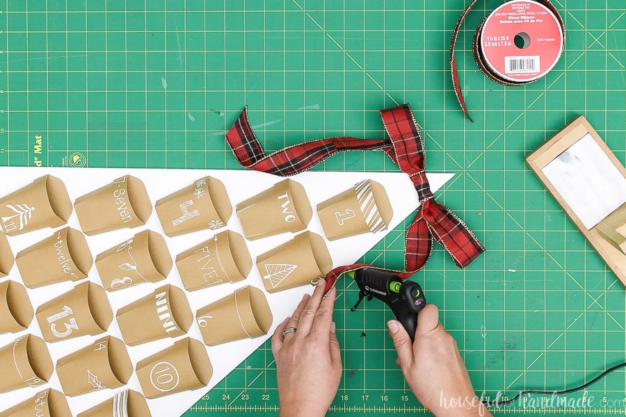 Glueing the sides of the ribbon tail to the sides of the Christmas tree advent calendar.