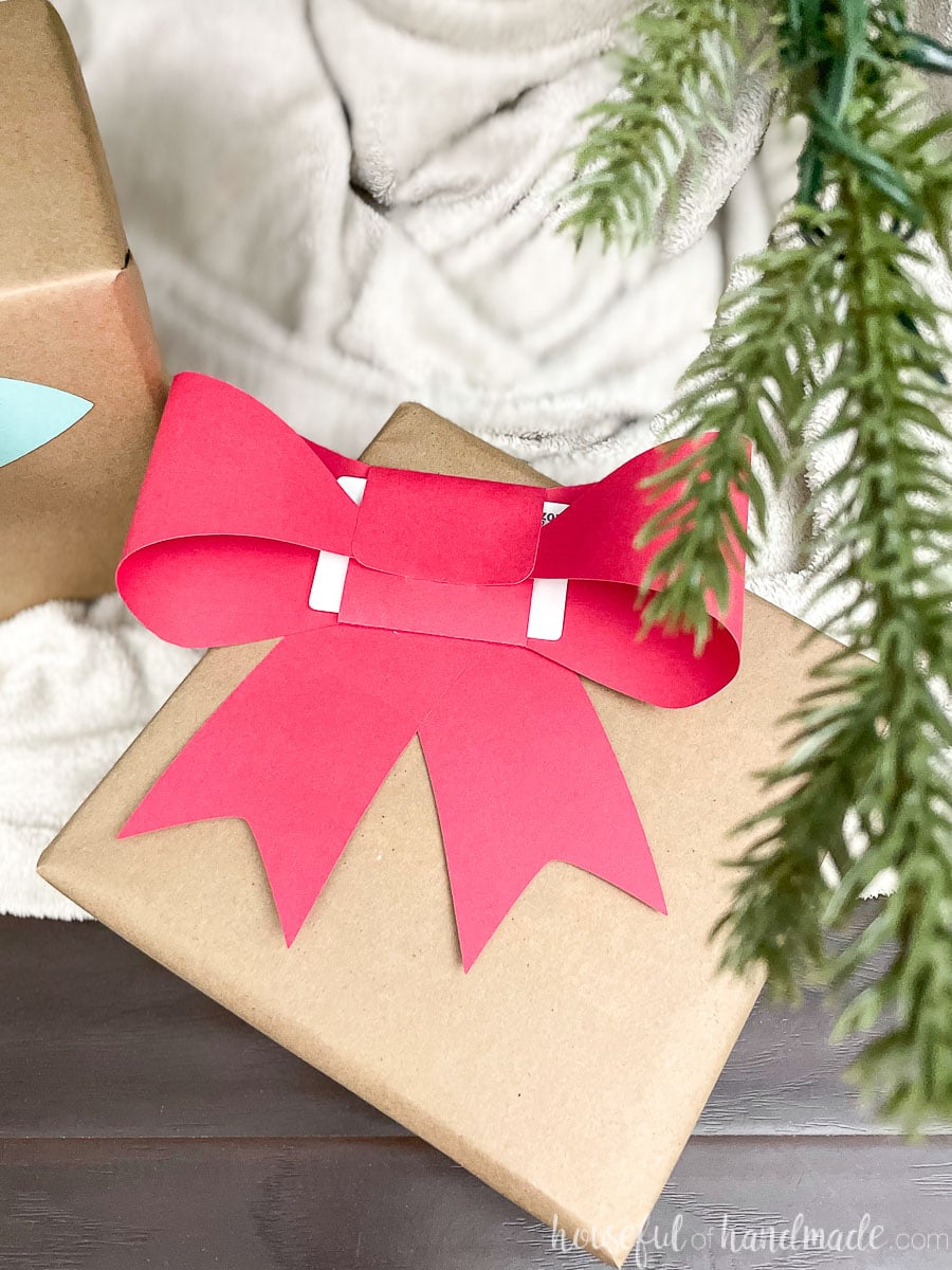 Christmas present under the Christmas tree with a red paper bow gift card holder on the front of it.