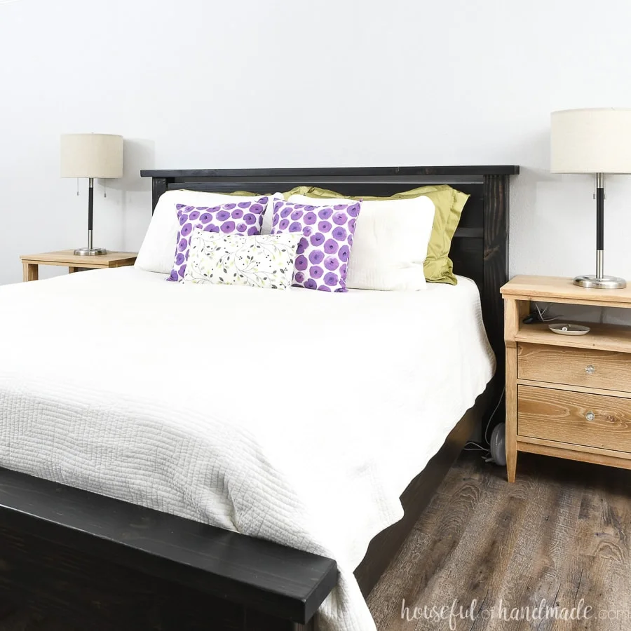 Black wood DIY bed frame for a queen bed dressed in a white comforter and colorful pillows.