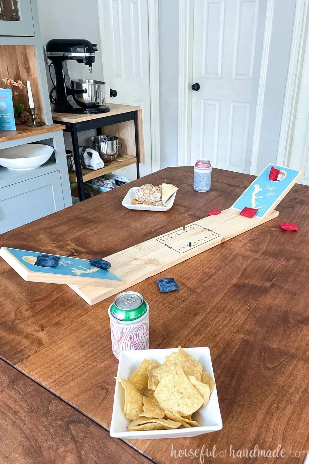 Dining room table with tabletop cornhole game made from wood on the table with drinks and snacks around it. 