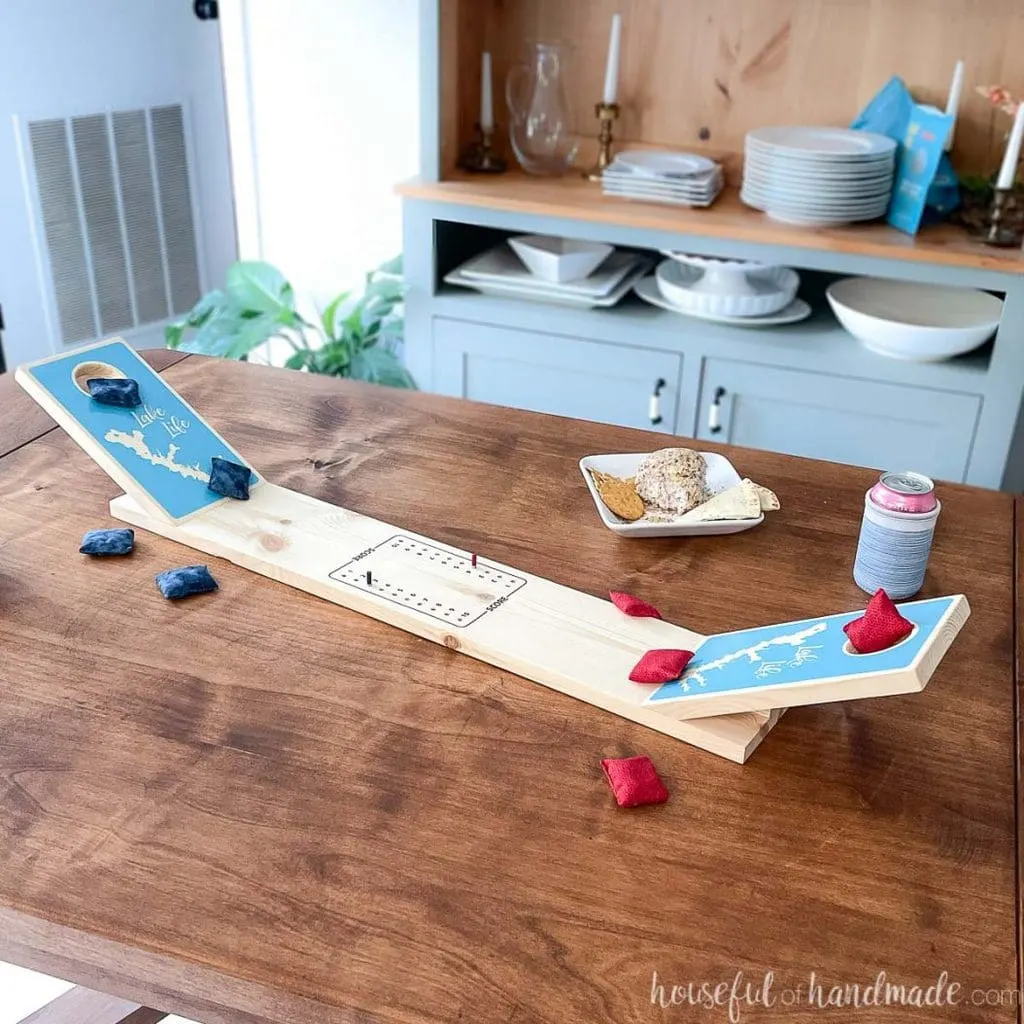 DIY tabletop cornhole board on a table with red and blue mini bean bags and snacks around it.