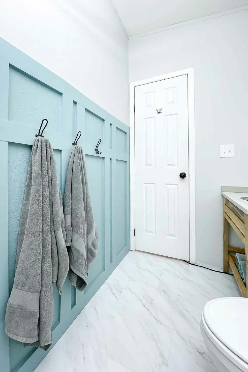 Looking toward the door of the small bathroom with board and batten wall and marble vinyl floor tiles. 