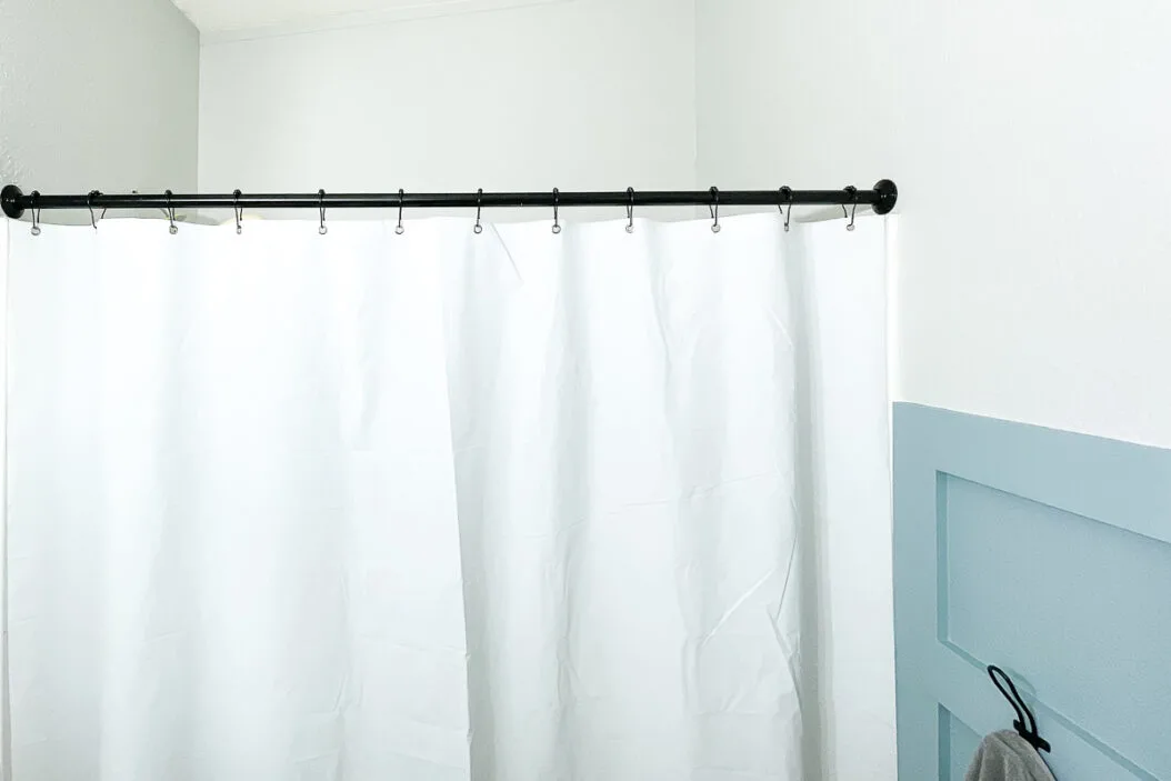 Black shower curtain rod with black rings holding a white shower curtain in the bathroom. 