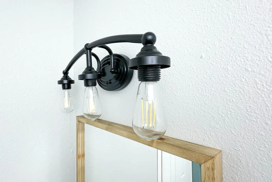 Black three bulb light fixture over the vanity mirror in the bathroom with no decorative glass and Edison bulbs inside. 