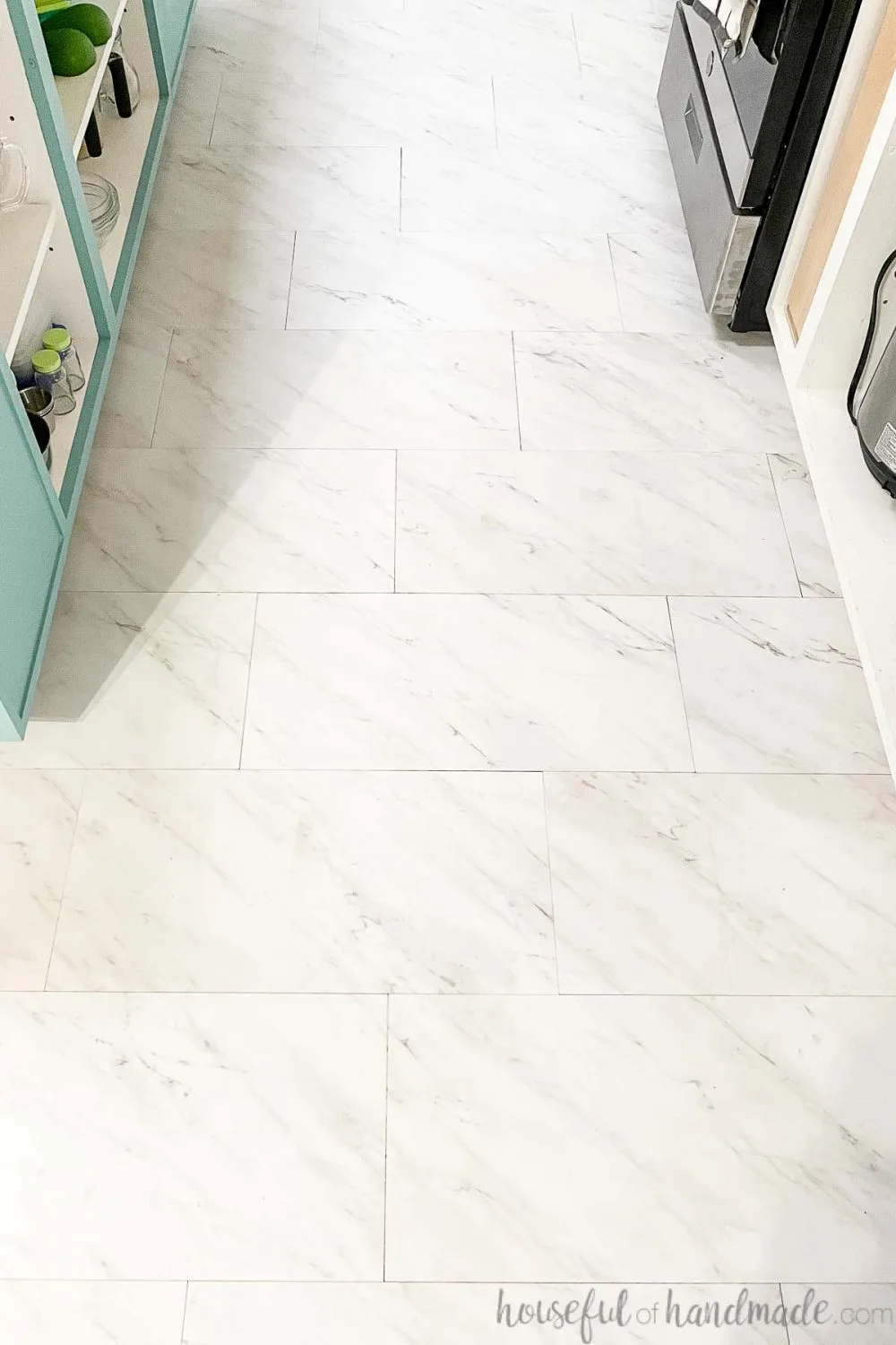 White vinyl tiles that look like marble laid in the kitchen between the sea green island and white cabinets.