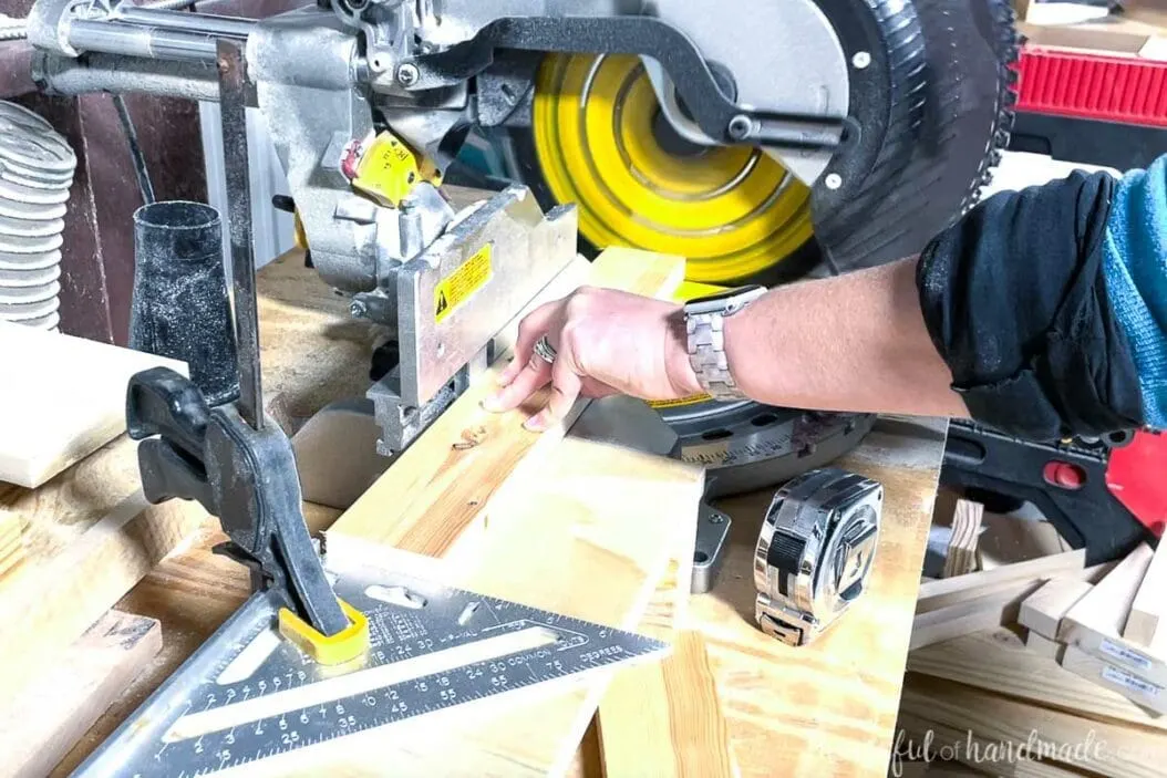 Cutting a 1x3 board on a miter saw with a speed square clamped to the table as a guide.