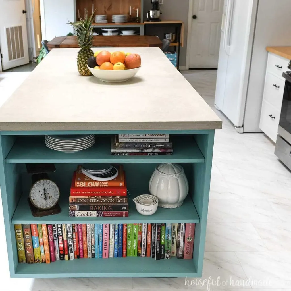 End view of the kitchen island with a concrete countertop and a dining room in the background. 