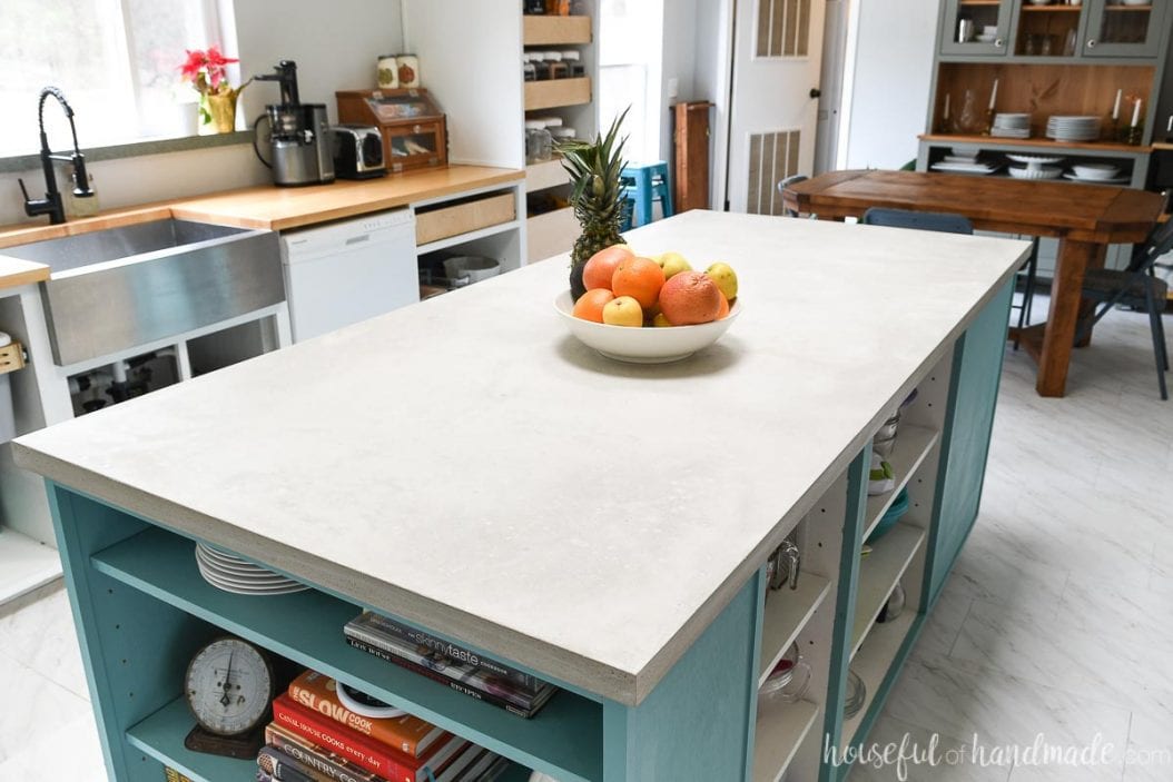 Kitchen with a large colorful kitchen island with a light gray concrete countertop and wood countertops on the white base cabinets.