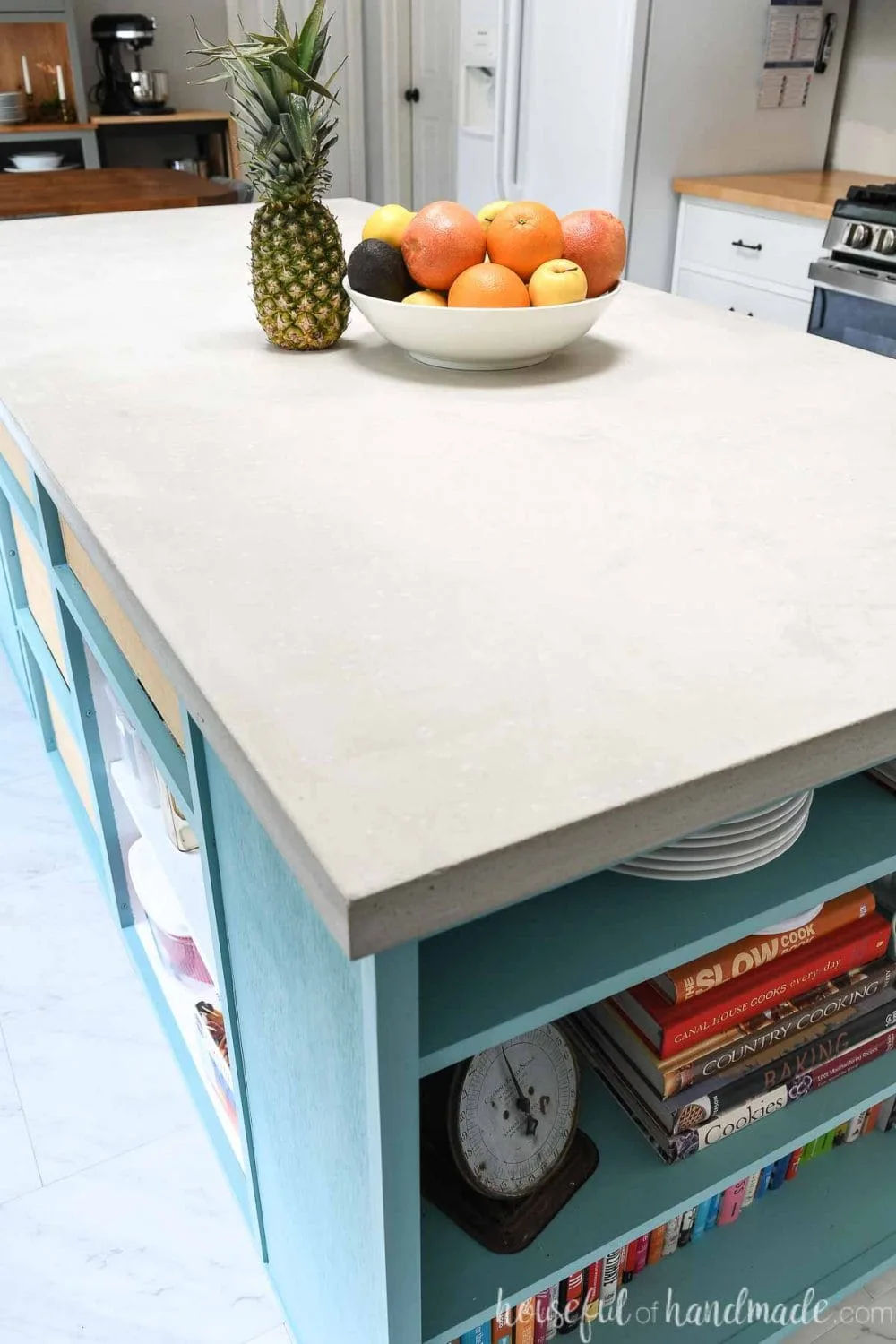 Looking down on the kitchen countertop made from light colored concrete on a blue kitchen island with a bookcase in it. 