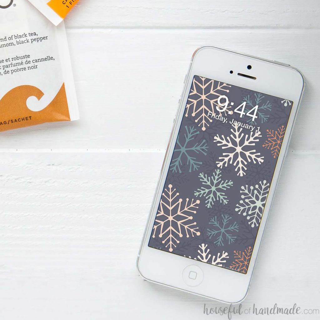 Bold snowflake digital wallpaper on the screen of a white iPhone sitting on a white table.