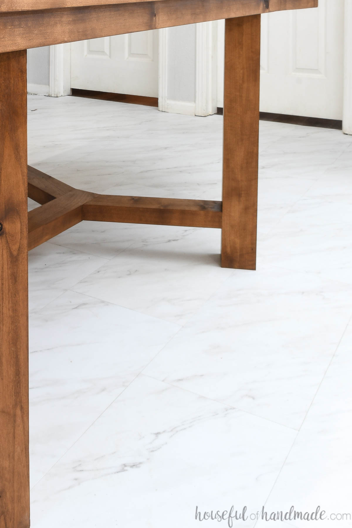 Close up of the grecian marble look vinyl tile installed in the dining room under a rustic table. 