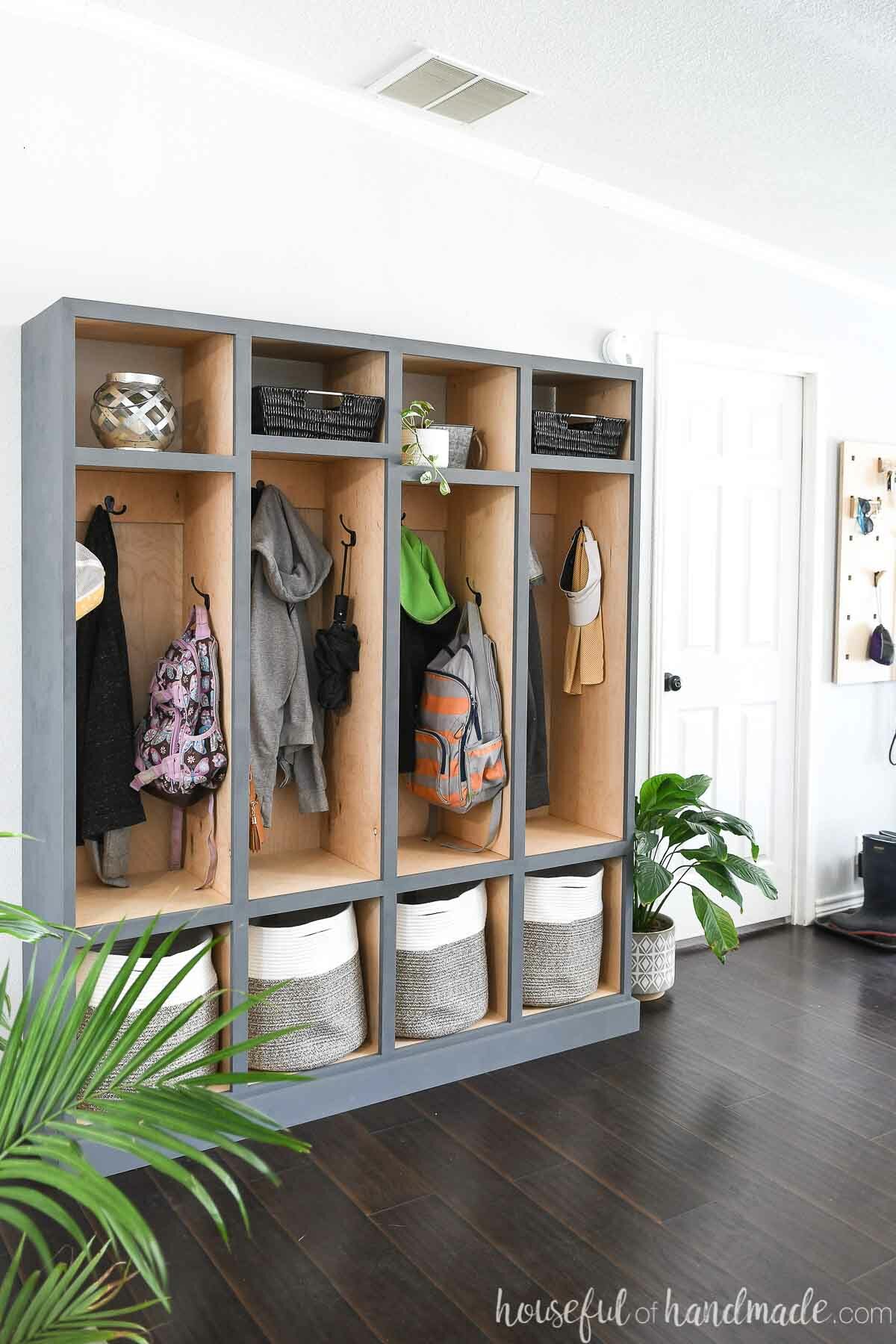 DIY mudroom storage lockers with natural wood tone on the inside and gray-blue painted outside in an entryway filled with coats and backpacks. 