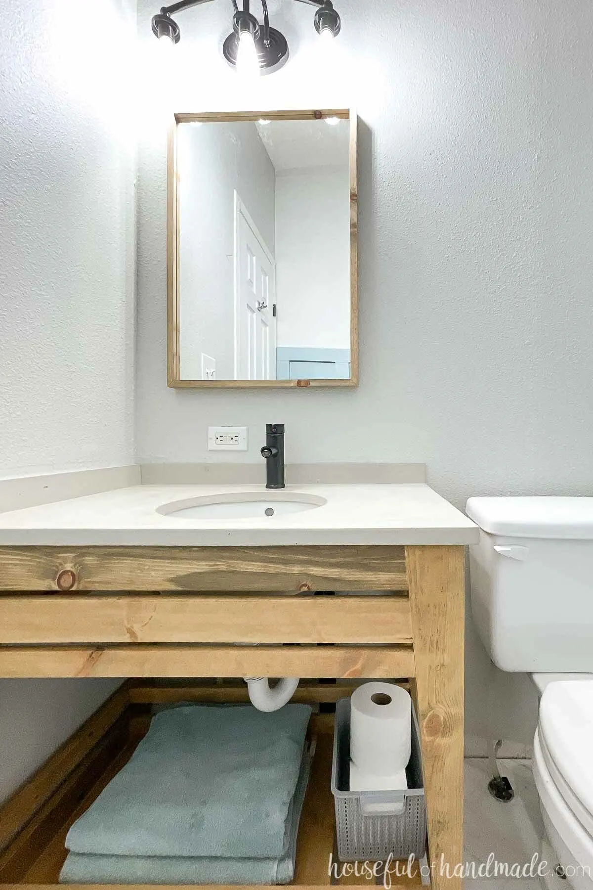 Open modern wood bathroom vanity with concrete vanity top, thin wood framed mirror and black fixtures in a bathroom. 