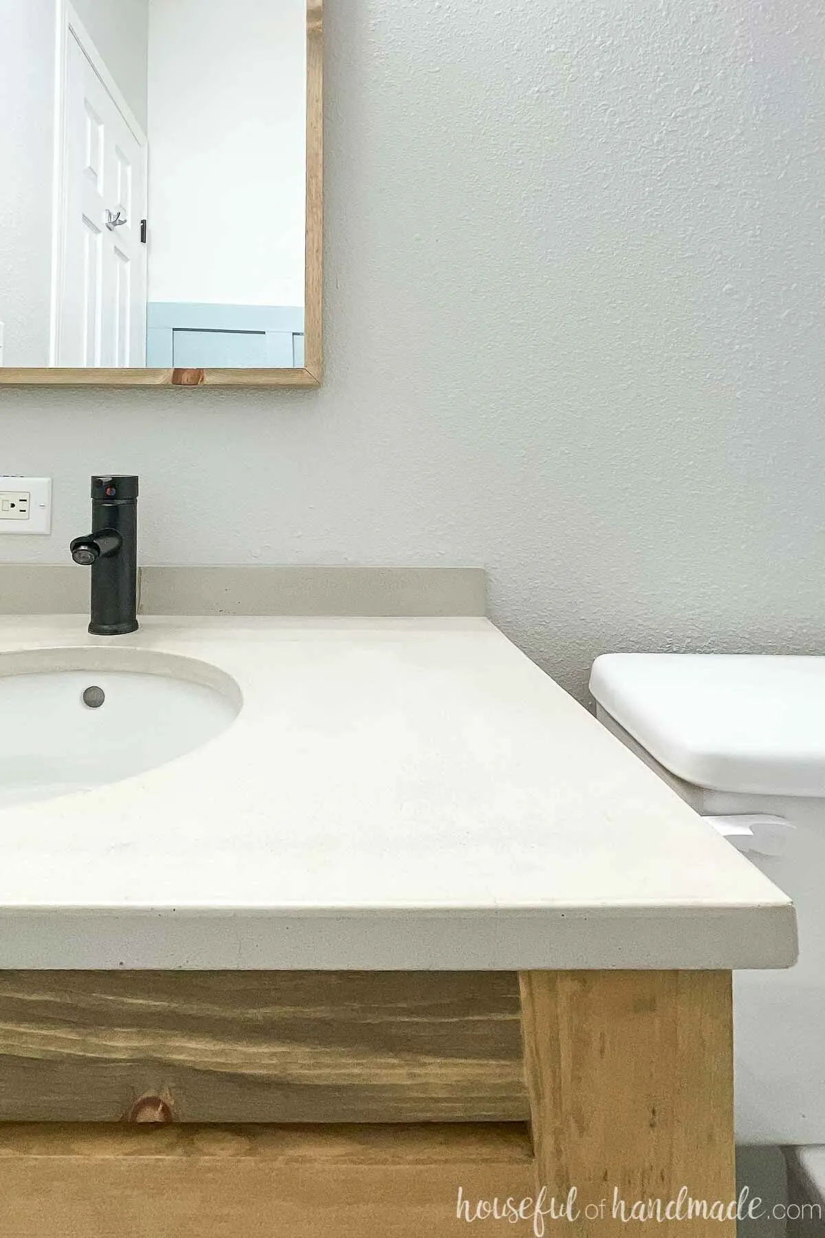 Half of the DIY concrete countertop installed on an open vanity with a black faucet and white undermount sink.