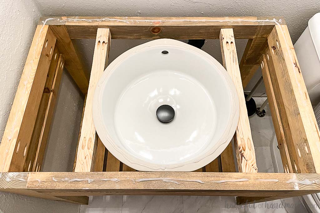 Open vanity with an undermount sink held up by 2x2 scraps with silicone on the vanity and sink waiting for the concrete vanity top. 