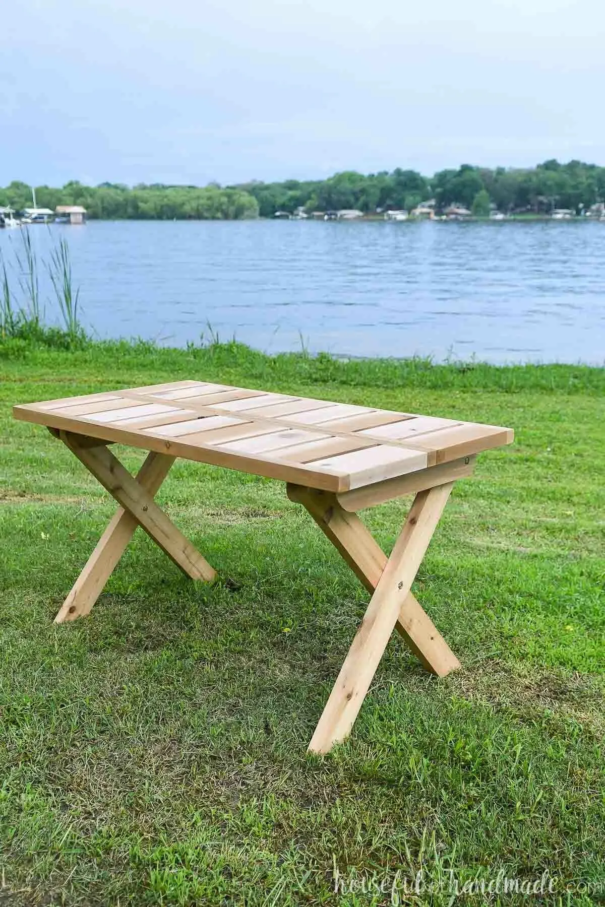 Cedar folding picnic table set up on the grass in front of a lake. 