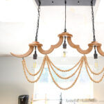 DIY wood chandelier with three light bulbs in a row and loops of wood beads draped below it.