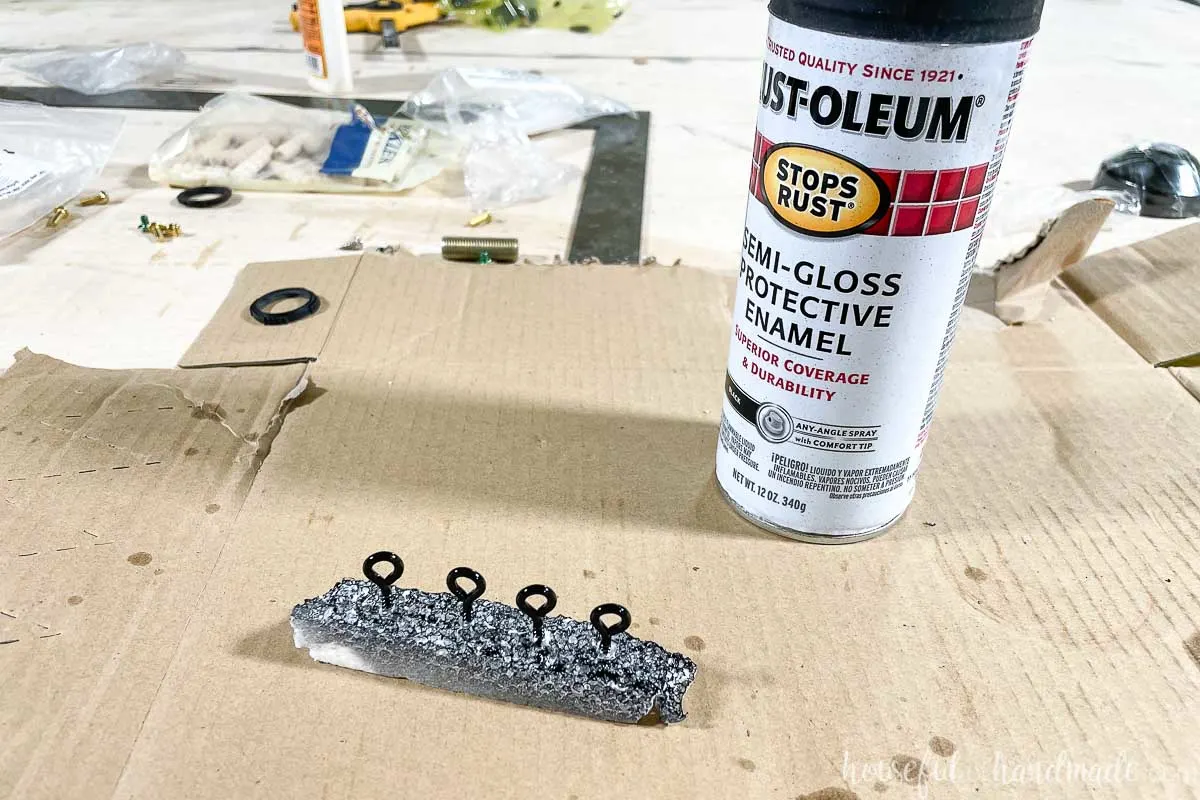 Four screw eyes in a piece of foam spray painted black next to a can of spray paint. 