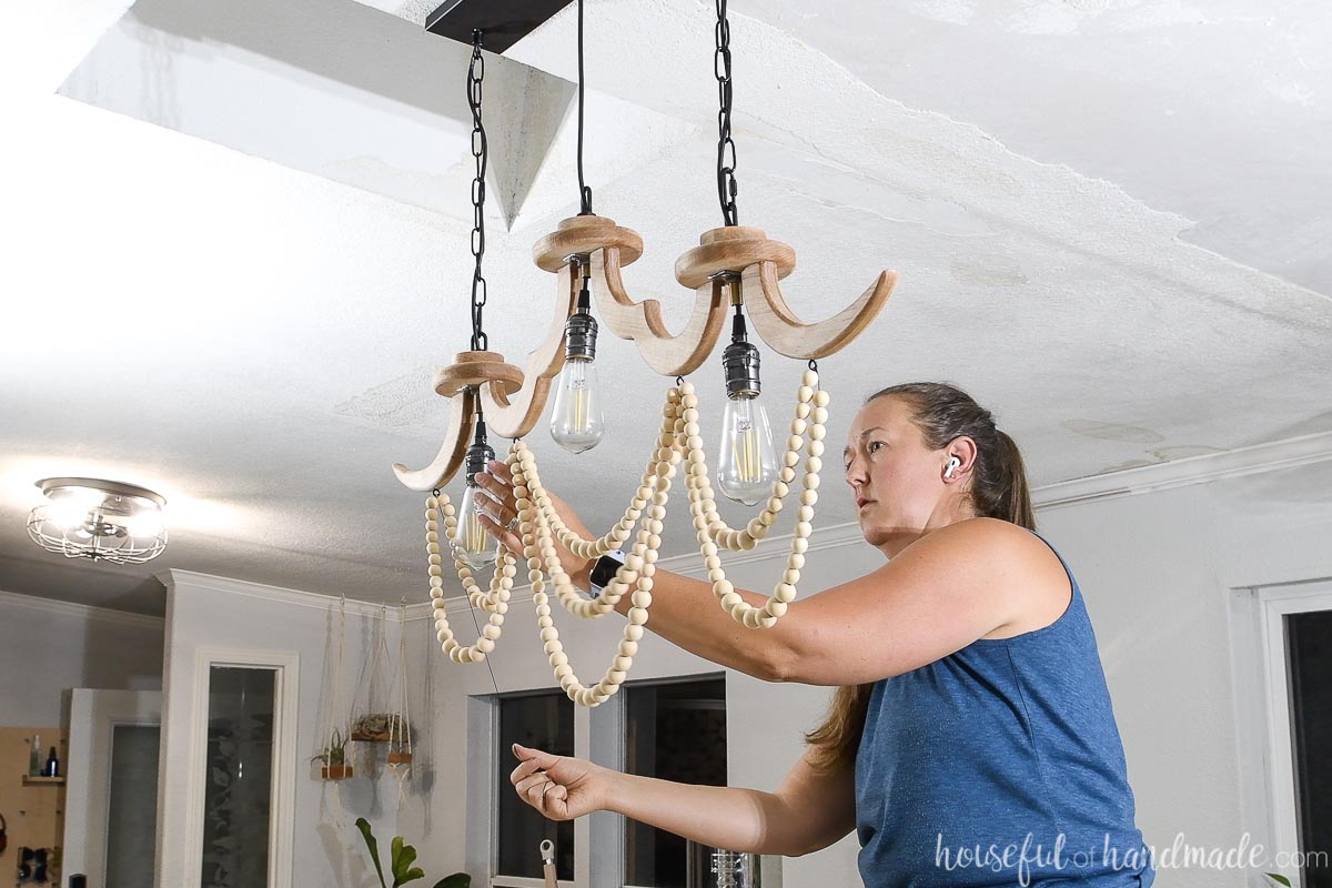 Threading beads onto black cording and tying to eye screws on the underside of the wood chandelier. 