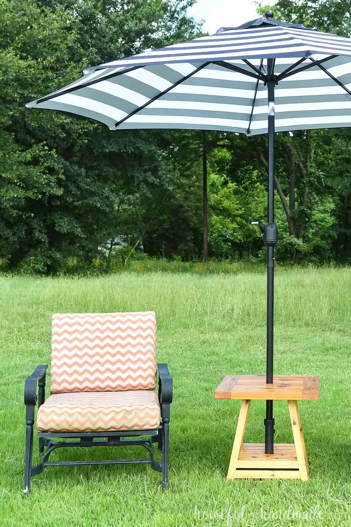Umbrella side table set up on the lawn next to an orange and white cushioned chair. 