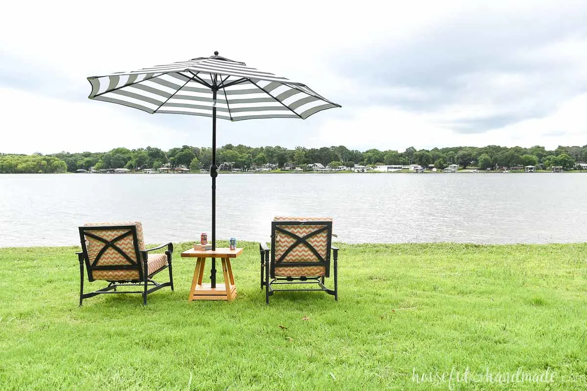 Two patio chairs sitting on each side of the umbrella side table overlooking a lake. 