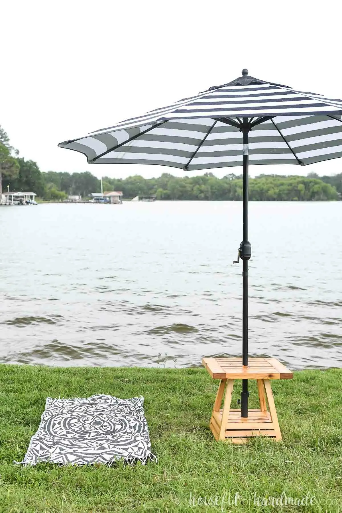 Small patio table with umbrella hole set up next to a beach towel by a lake. 