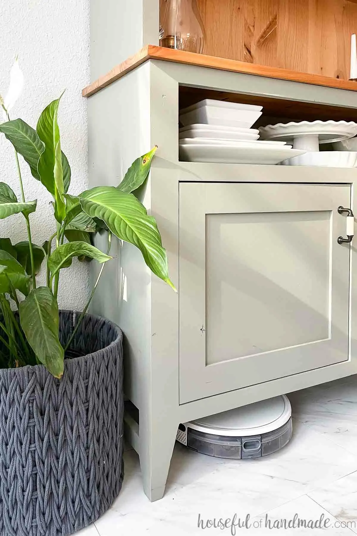 Green painted hutch with large clearance below to store a robot vacuum for charging with a plant next to it.
