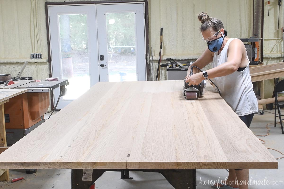 Sanding the flat oak table top with a belt sander.