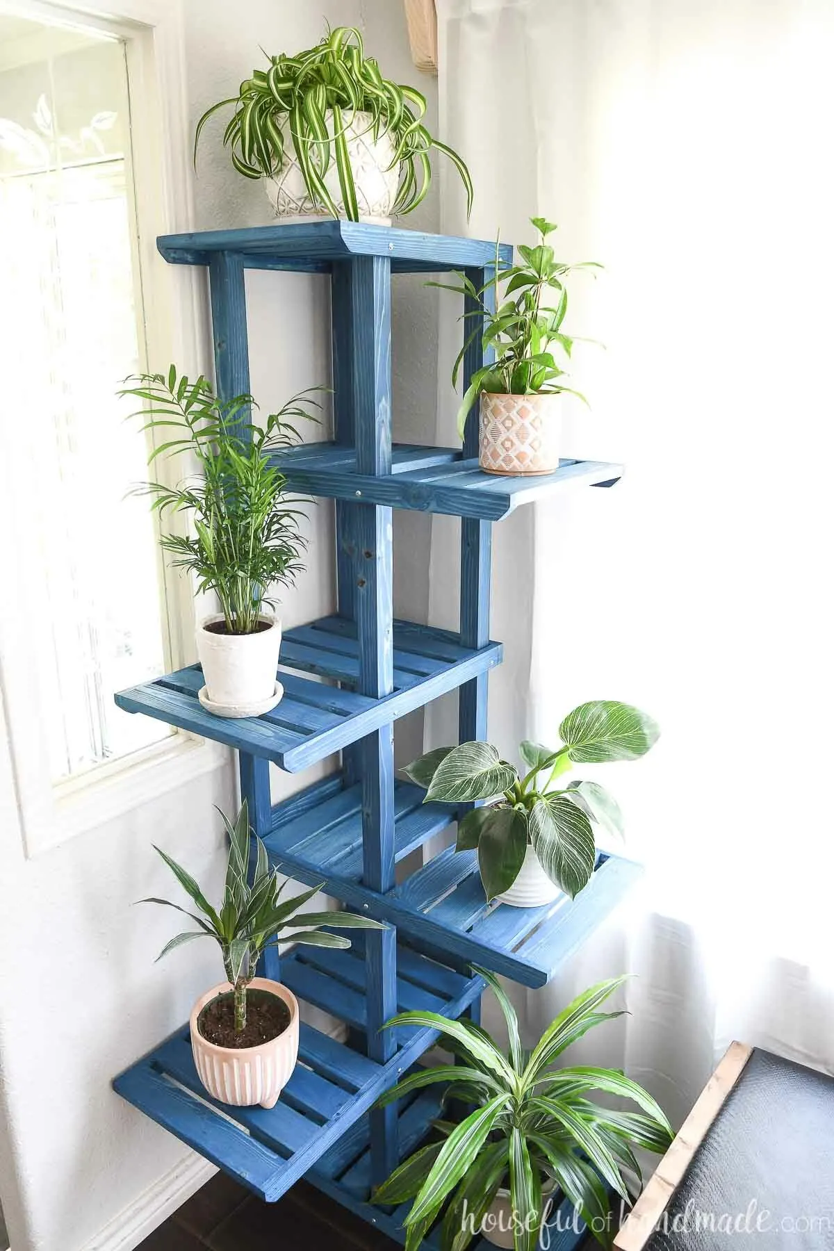 Blue stained plant stand with 6 large shelves in a corner. 