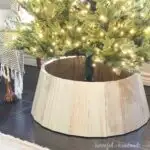 DIY wooden tree collar under a light up Christmas tree on a dark wood floor.