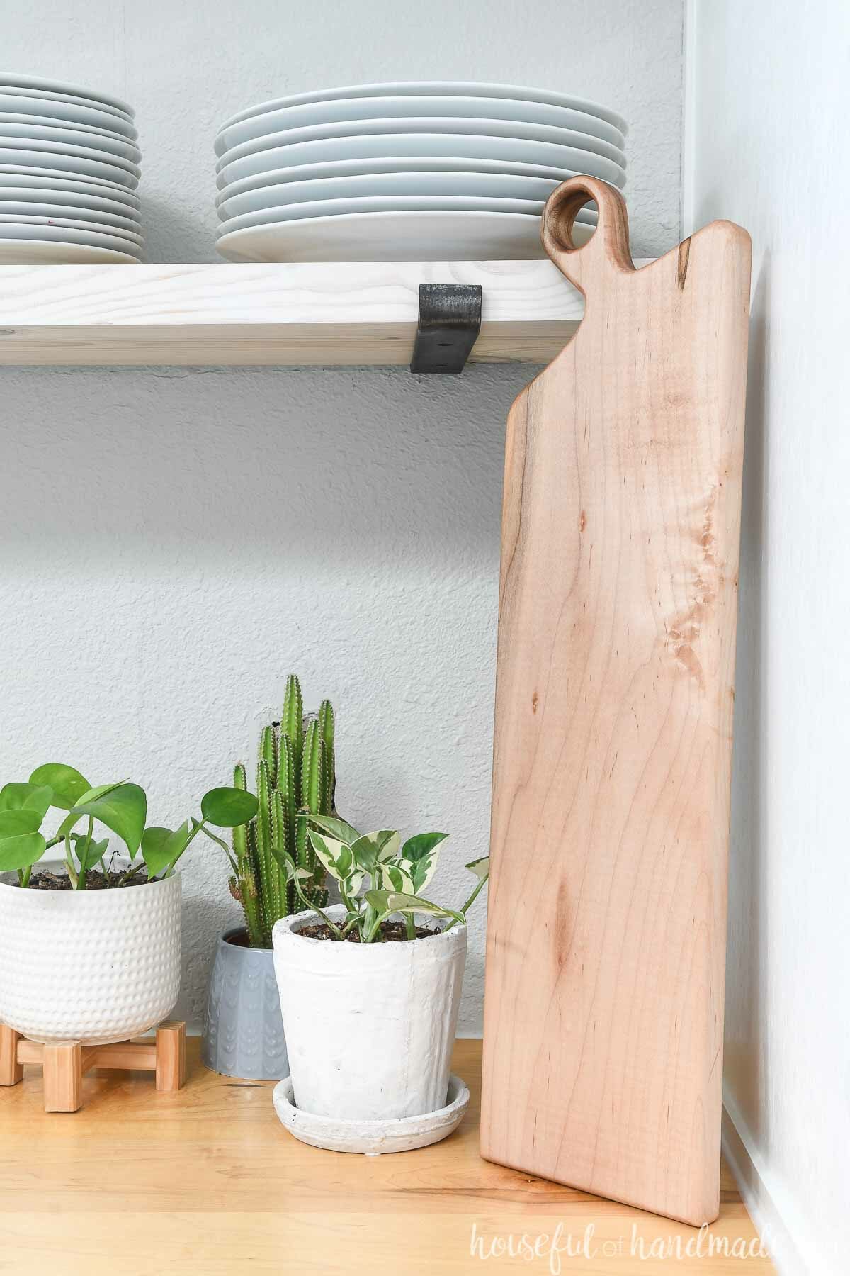 Long DIY breadboard made from maple leaning up against a cabinet and open shelves. 