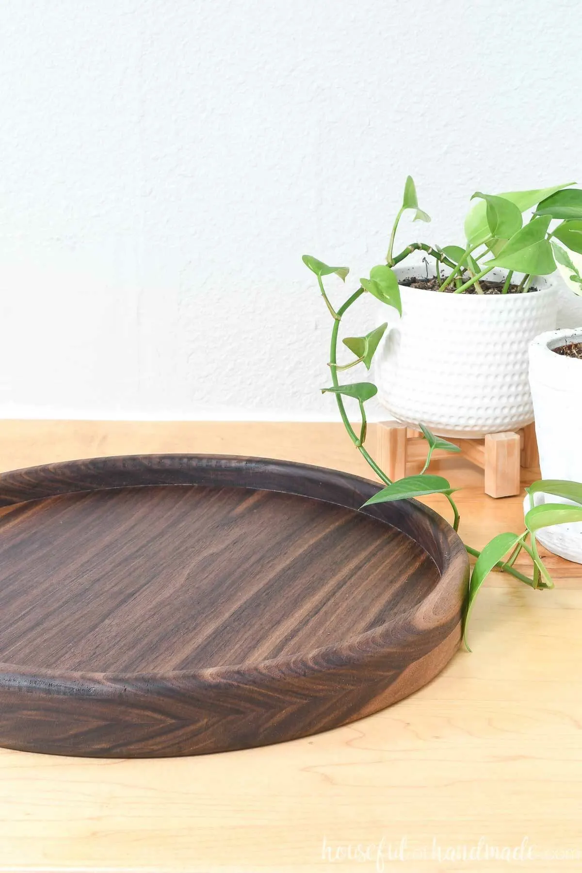 DIY round tray made out of walnut on a counter next to small house plants. 