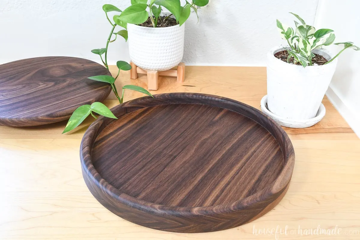 Round tray made from walnut wood with a smaller round tray made from the inside scrap sitting on a counter with two plants around them. 