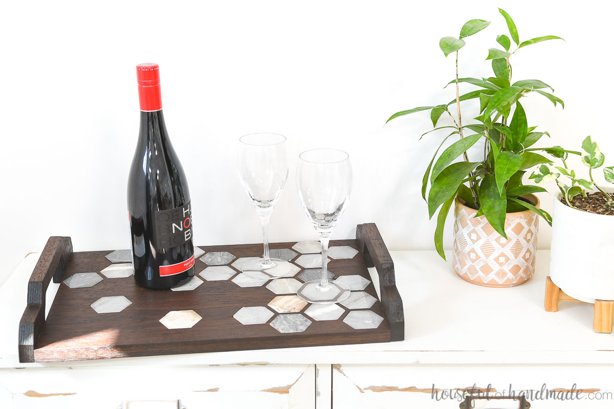 Wood and marble serving tray with handles serving drinks on a table. 